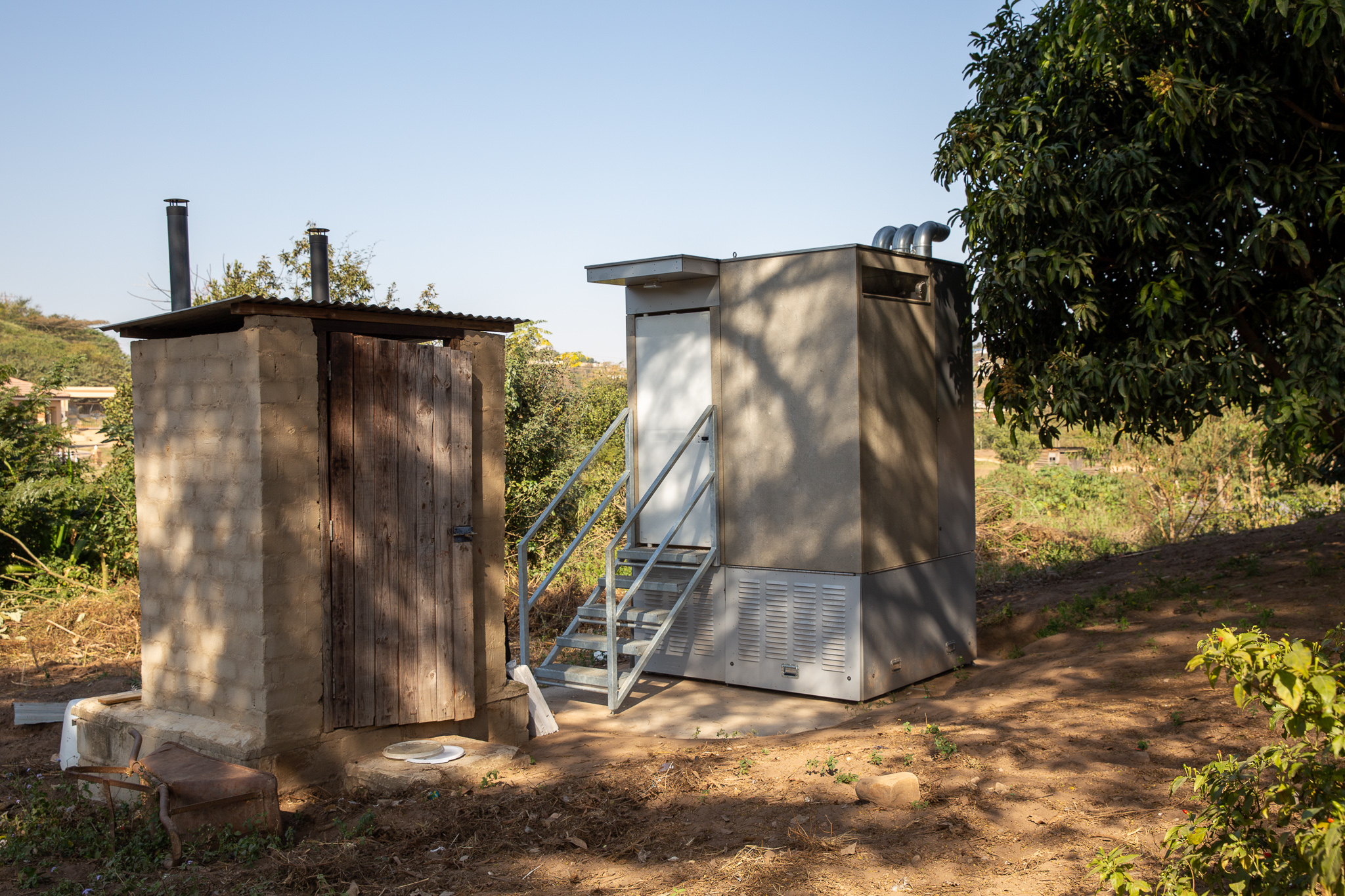 Essai sur le terrain du cabanon de toilettes autonome Blue Diversion Autarky toilet, avec séparation de l’urine, installé à côté de toilettes sèches existantes (à gauche) dans un jardin à Durban, Afrique du Sud. ©️ Autarky, IFAEPE