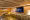 An interior view of the House of Switzerland, featuring a warm wooden lounge with bar seating, Swiss branding and a large screen displaying the hashtag #swisshouse.