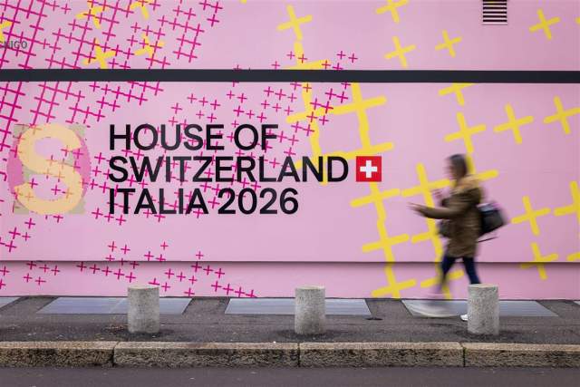 Pink building facade displaying the text “House of Switzerland Italia 2026,” with a passerby walking in front.