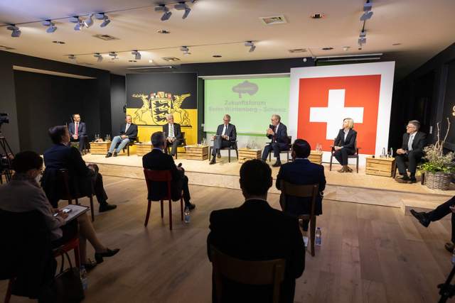 Panel discussion with Swiss flag in the background and Guy Parmerlin on the microphone