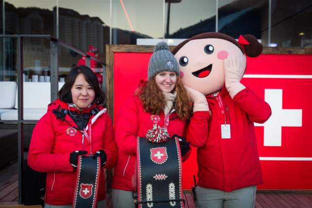 Two staff members posing with the Heidi mascot and traditional Swiss cowbells.