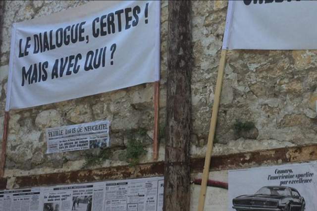 Photo installation at Rencontres d’Arles 2018, with French protest banners and vintage newspaper clippings displayed on a stone wall.