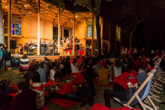 A lively evening concert at the House of Switzerland in Mexico, with visitors gathered around the wooden pavilion for a cultural performance.